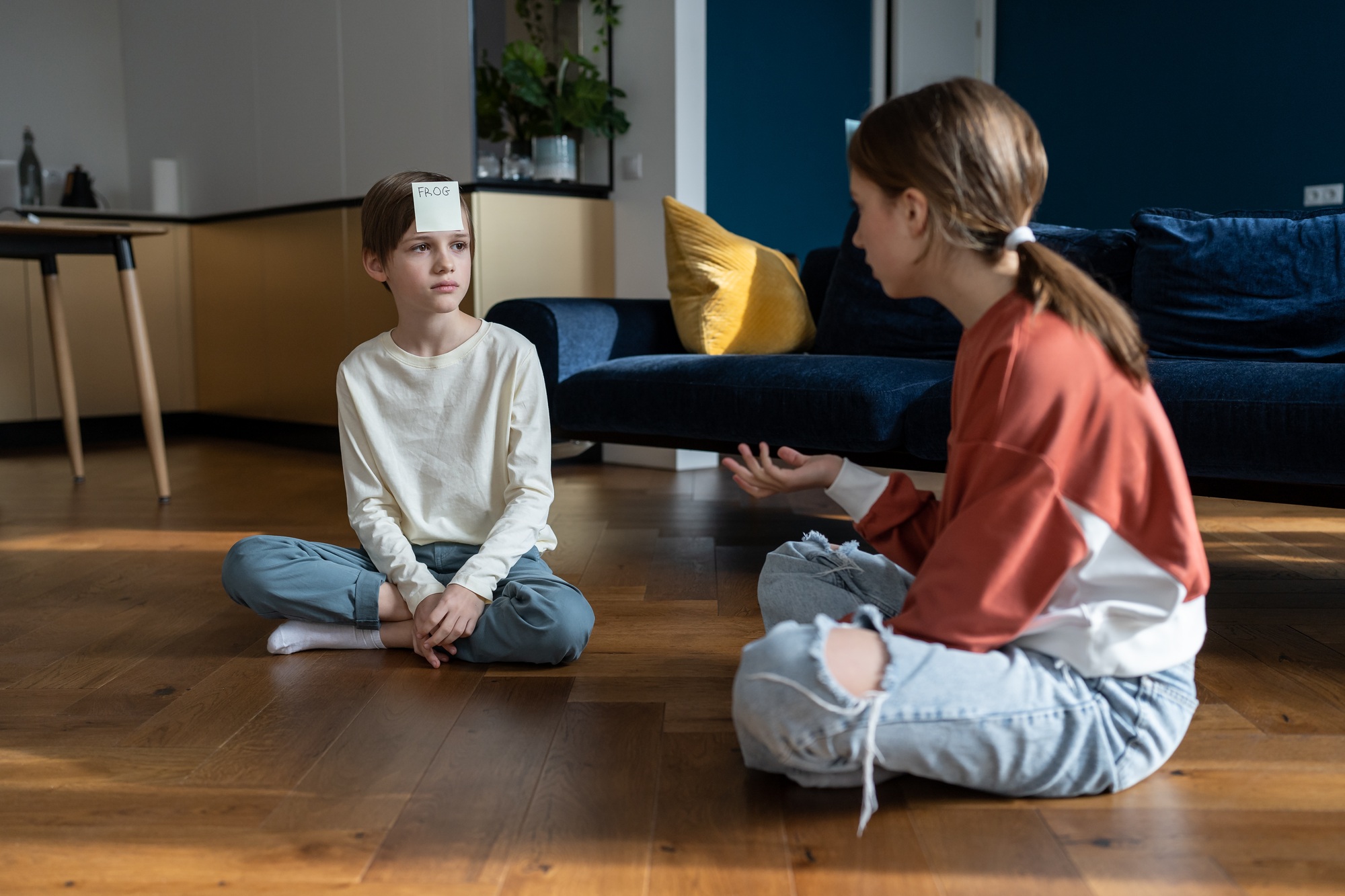 Small children boy and girl playing guessing game with sticky notes while sitting on floor at home