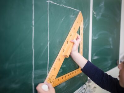 child draws line with chalk using triangle ruler on blackboard in school classroom