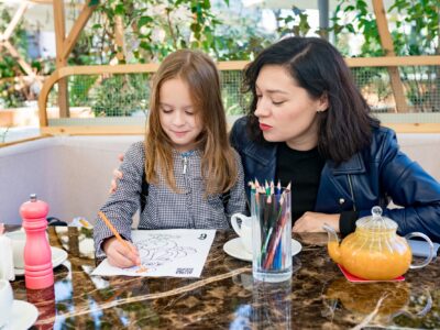 Child girl drawing coloring book in cafe