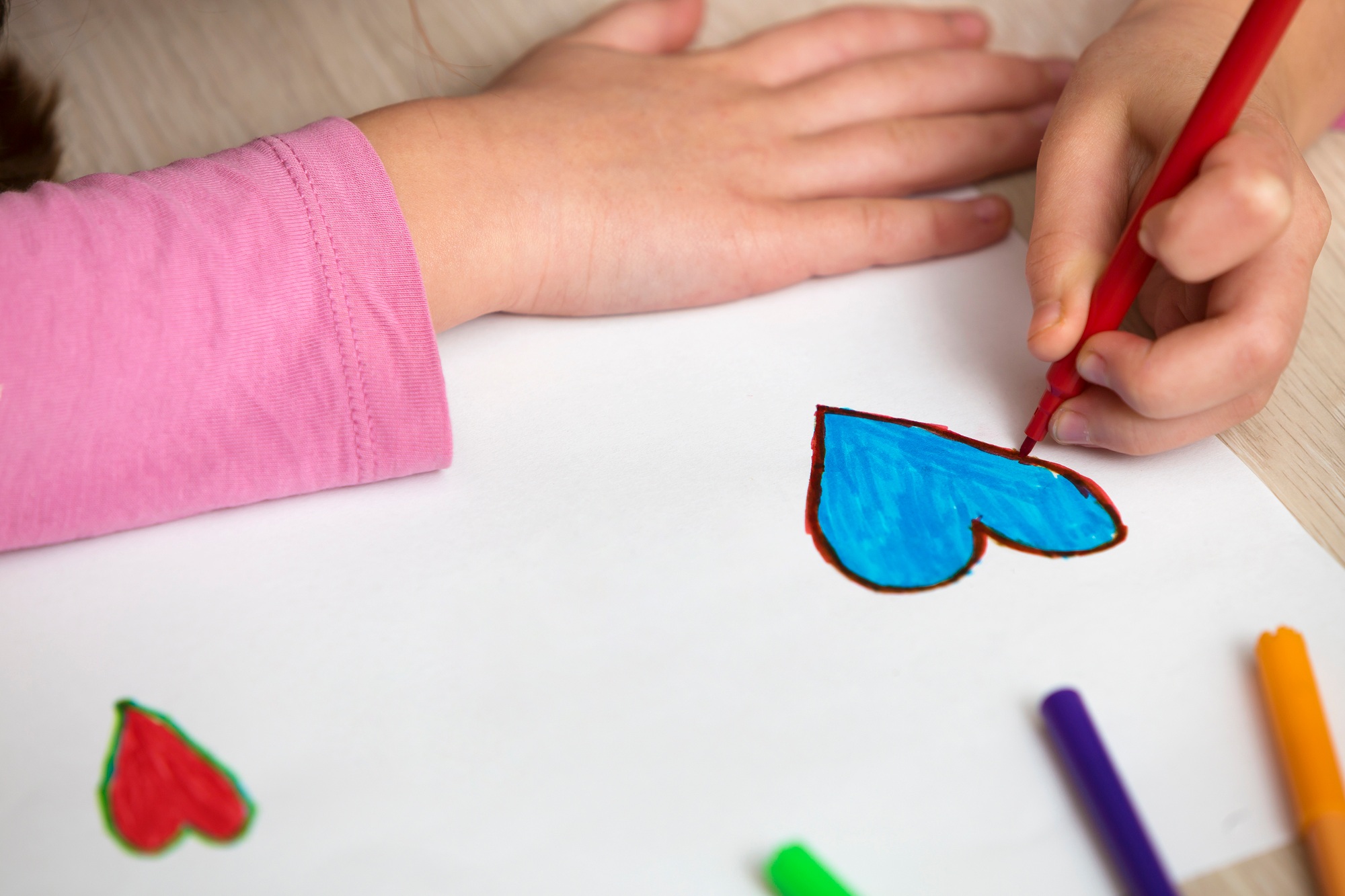Child girl hands drawing with colorful pencils crayons heart on white paper.