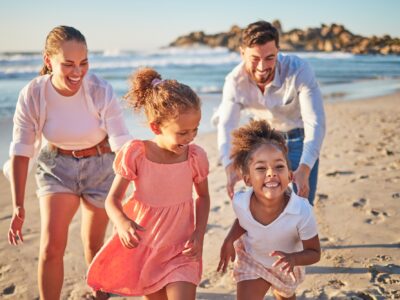 Ocean, holiday and happy family running on beach on a summer vacation. Mom, dad and girl children l
